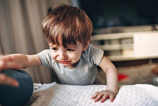 A toddler is crying and reaching for something on a couch