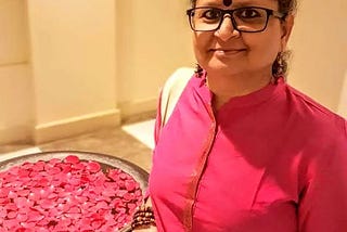 Woman in pink kurta wearing glasses, standing next to rose petals