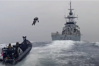 A Royal Marine in a jet pack launches from a fast boat to board a Royal Navy ship. Agile in action.