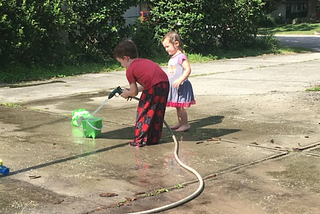 Photo of two of the author’s young children playing with a hose and bucket of water on a driveway.
