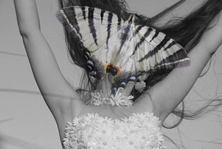 A model stands, arms up, with moth wings edited over their face.