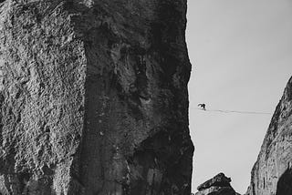 A black and white photo of tightrope walker between two cliffs