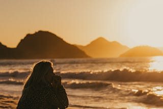 A woman sitting on the sand at the beach staring into the horizon.