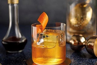 Old Fashioned Cocktail in a Modern Glass with a Large Ice Cube and Orange Twist