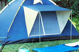 A tent surrounded by trees with a sleeping bag, cooler and camping chair