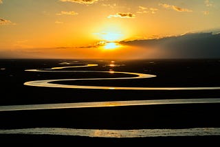 A winding river, with the sun going down behind the plains.