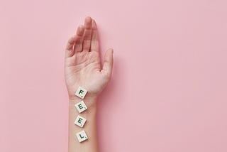 A hand with scrabble tiles on the wrist spelling “feel”