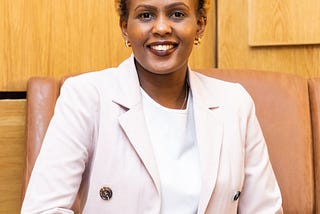 Professional headshot of VestedWorld Vice President, Keziah Njeri. Seated on brown leather chair, wearing a suit