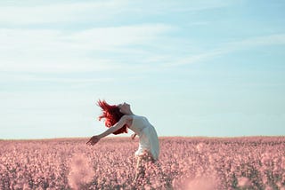 A woman moving freely in a field of pink flowers.