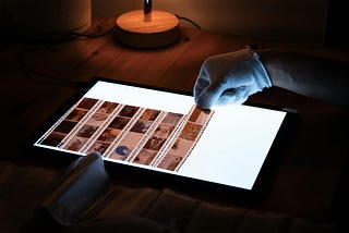 a photo of a gloved hand adding cut filmstrips to the top of a darkroom lightbox