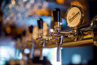 Six beer taps receding in focus towards a blurry window to daylight