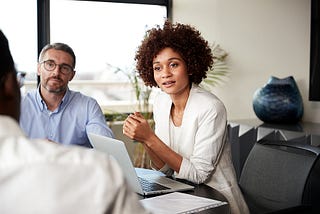 A millennial women in a conference room talking with two male colleagues.