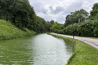 The photo shows a long pond with a walking and cycling path next to it.