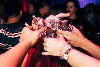 A group of people’s hands holding up shot glasses