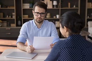 Young man dressed in a blue shirt with a puzzled look on his face as he looks at the woman sitting across the table from him.