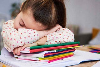 Little girl falling asleep at her desk on top of her school workbooks.