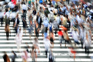 A crowd of people walking in a crosswalk on a busy city street