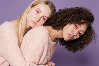 One woman hugs and leans on the back of her friend.