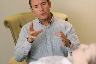 A man sitting in a chair is talking to a woman who is lying on a couch in an office.