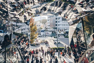 People walking through a mirrored urban space in Tokyo, with reflections creating multiple overlapping perspectives that symbolise individual journeys within a larger social system.