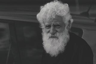 Older gentleman with white hair and beard looks at the camera