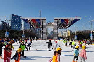 Young ice skaters skating with the Peace Gate behind them.