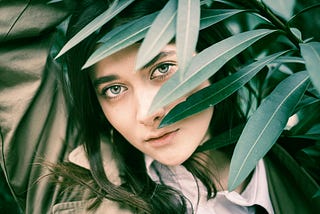 A woman looks out from behind green leaves.