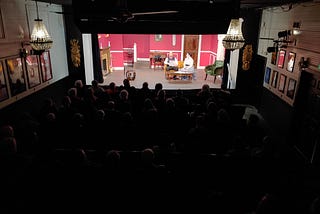 Two actors on a theatre stage, with a rapt audience watching on