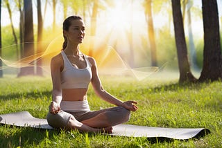 A woman, sitting cross-legged on a yoga mat in a serene forest clearing