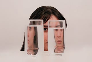 Girl hiding behind two full glasses of water that distort her perception