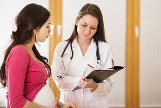 A young woman consults with her doctor, who is listening to her.