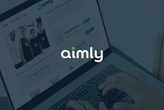 Photo of a person on a laptop checking fundraising progress on goaimly.com behind a faded dark blue background with the aimly logo front and center.