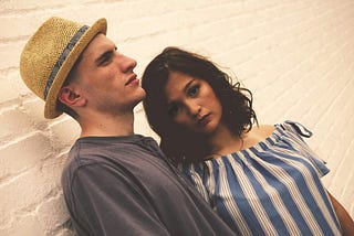 A man and woman stand together against a white brick wall