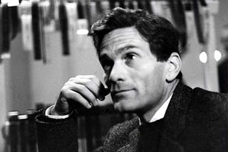 Em primeiro plano, Pier Paolo Pasolini olha para cima. Em segundo plano, vários negativos de fotos estão pendurados e secando em varais.