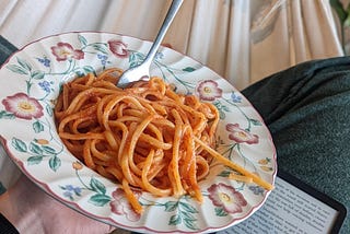 Myself holding a plate full of Amatriciana next to my kindle reader. The plate looks like an old fashion Nona plate with painted flowers, some would say ugly, I would say my favorite kind of plate.