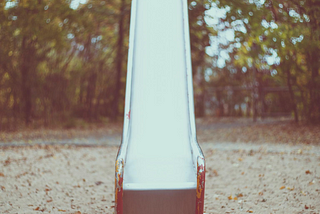 A metal slide on a sunny day, surrounded by trees.