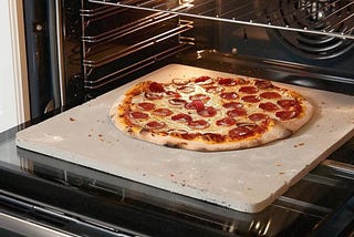A pizza baking on a pizza stone in a home oven.