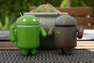 a green clay model of android bot and a earthen colored clay model of another android bot are standing next to each other on a table.