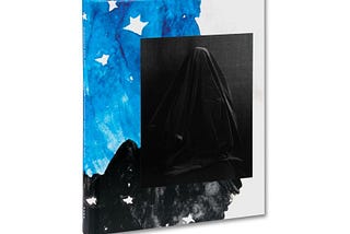 A photograph of the cover of Who Is Changed and Who Is Dead, Ahndraya Parlato’s monograph. The cover has a dark, black-and-white photograph of a woman covered with a dark piece of cloth, recalling Hidden Mother photographs of the 19th Century. The background behind the photograph is water color, with a large bright blue section and a smaller black section, with white stars interspersed.