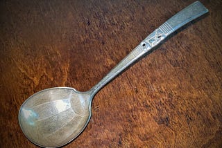 Large tarnished and scratched silver gravy ladle against a wood background.