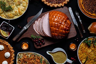 Christmas dinner on a table with ham, stuffing, gravy, and several pies.