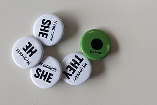 Assorted White Pronoun Badges and a Single Green Communication Badge on a White Background