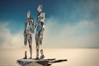 An art installation representing two human figures holding hands, made of mirrors, in the middle of Nevada Desert.