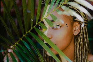 Black woman poses behind leaves.