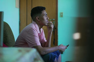 Young man sitting with hand on chin, smartphone in other hand
