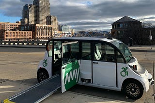 An autonomous May Mobility shuttle with a wheelchair ramp deployed at a stop in Grand Rapids, Michigan.