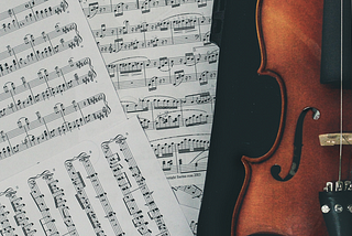 A violin in a black case, lying on top of some scattered sheets of musical notation.