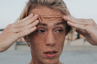 Photo of a man with blond hair and freckles holding the sides of his head looking stressed out.
