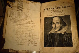 An old, yellowed book opened up to the title page: a handwritten page is layered on the left; on the right the title page “Mr. William Shakespare, Comedies, Histories, and Tragedies” with his portrait (looks like engraving).