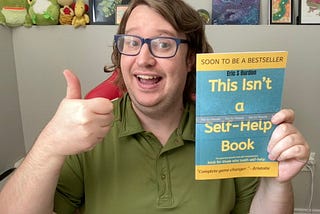 Myself holding up my latest book “This Isn’t a Self-Help Book” with a thumbs up and smiling.